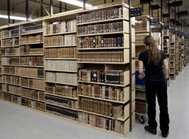 Collectiebehoud: een magazijn van de KB, met rijen boekenkasten en een medewerker die erlangs loopt.