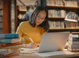 Vrouw doet onderzoek in bibliotheek achter laptop met boeken