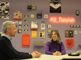 Een man en een vrouw voor een muur met oude computers, onderdelen en tijdschriften
