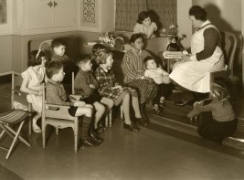 Zuster leest voor aan groep kinderen. Programma Indisch Erfgoed Digitaal.