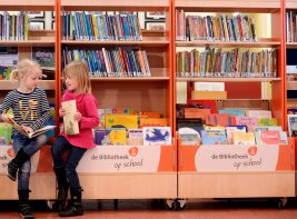 Twee kinderen die op een bak boeken zitten te lezen
