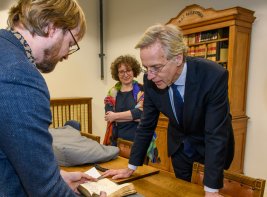 Collectiespecialist Jeroen Vandommele toont minister Dijkgraaf een boek uit de collectie, algemeen directeur Lily Knibbeler kijkt toe.