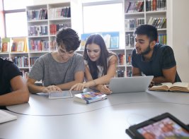 Students read on tablet, laptop and in a book in a library.