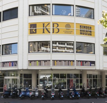 Image accompanying an article about reserving a workplace in the KB. Photo of the main entrance of the KB, with the logo of the KB and the Children's Book Museum on it.