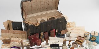 Miniatuurkist van de familie Cornets de Groot. De kist staat open en ervoor liggen spullen uitgestald, waaronder een landkaart en een aantal kleinere doosjes..