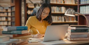 Vrouw doet onderzoek in bibliotheek achter laptop met boeken