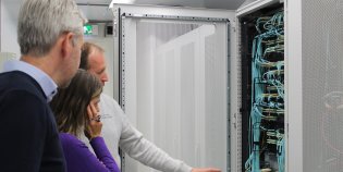 Twee mannen en een vrouw voor een serverkast vol kabels