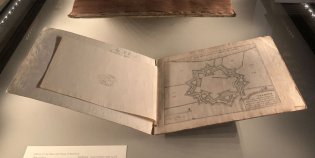 Een lange hal met in het midden glazen vitrines met opengeslagen boeken, aan de zijkanten rijen van bustes.