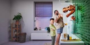 Een vader die schrikt van een dinosaurusschedel aan de muur. Naast hem lacht een kind. Aan de muur hangt een octopus met een bril.