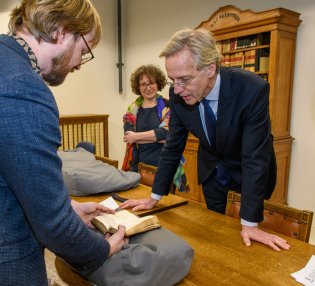 Collectiespecialist Jeroen Vandommele toont minister Dijkgraaf een boek uit de collectie, algemeen directeur Lily Knibbeler kijkt toe.