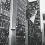 Man op ladder tegen een boekenkast aan.