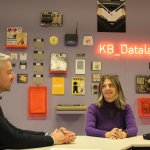 Een man en een vrouw voor een muur met oude computers, onderdelen en tijdschriften