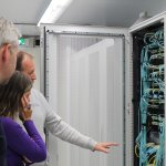 Twee mannen en een vrouw voor een serverkast vol kabels
