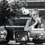 Een zwartwitfoto van Willem Oltmans die zit te roken voor een kast vol met tientallen banden van zijn dagboeken.
