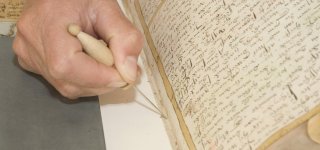 In het kader van collectiebehoud wordt een boek gerestaureerd. Op de afbeelding worden naaigaten voorgeprikt in een oud boek.