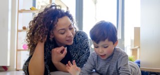 Vrouw en kind liggen op de grond en kijken samen naar een tablet.
