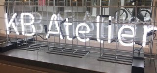 Voor het raam van de KB staan in lichtgevende letters de woorden KB Atelier geschreven.