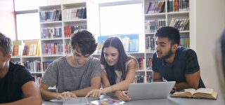 Students read on tablet, laptop and in a book in a library.
