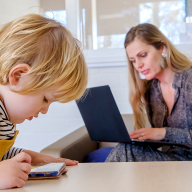 Volwassene en kind. Volwassene heeft een laptop op schoot, kind leest een boekje.