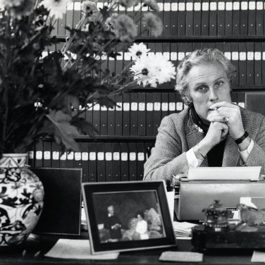 Een zwartwitfoto van Willem Oltmans die zit te roken voor een kast vol met tientallen banden van zijn dagboeken.